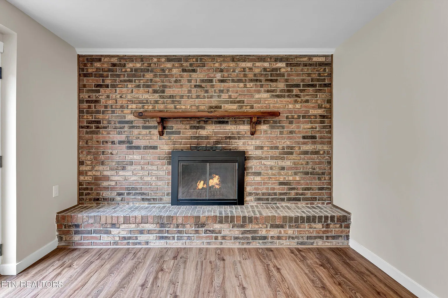 Full-wall brick fireplace with wood mantel shelf and hardwood flooring in a custom-built home
