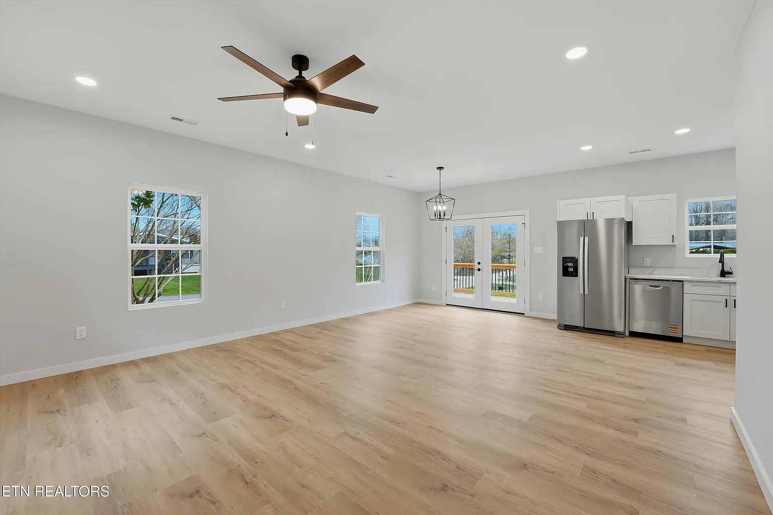 Spacious open floor plan with LVP flooring, recessed lighting, ceiling fan, and French doors to deck