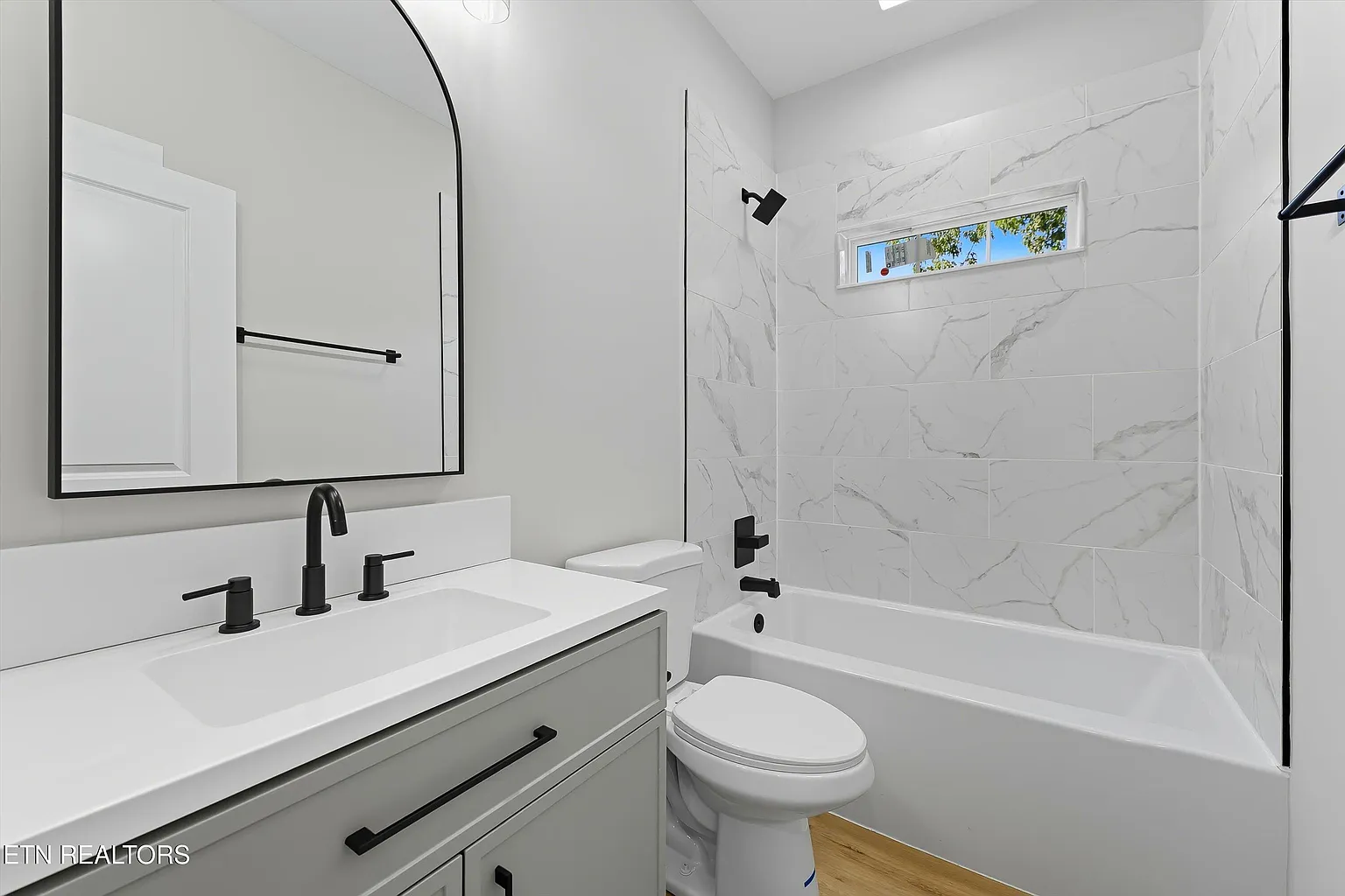 Modern bathroom with marble-look tile surround, matte black fixtures, and vanity with arched mirror
