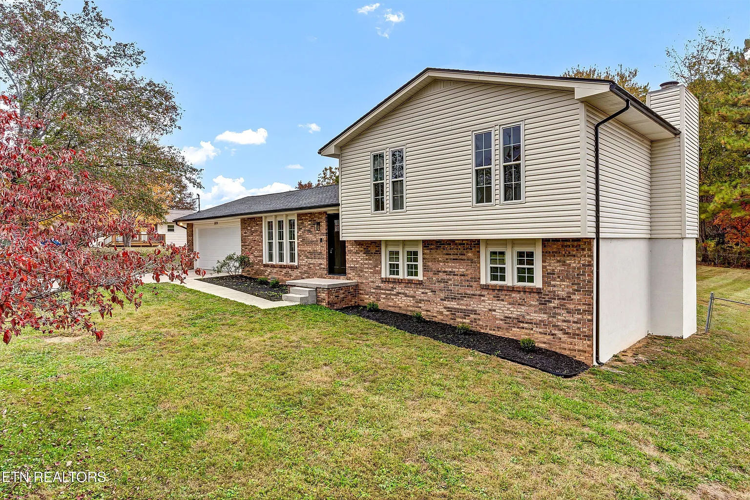 Renovated split-level home with brick and vinyl siding, attached garage, and landscaped front yard